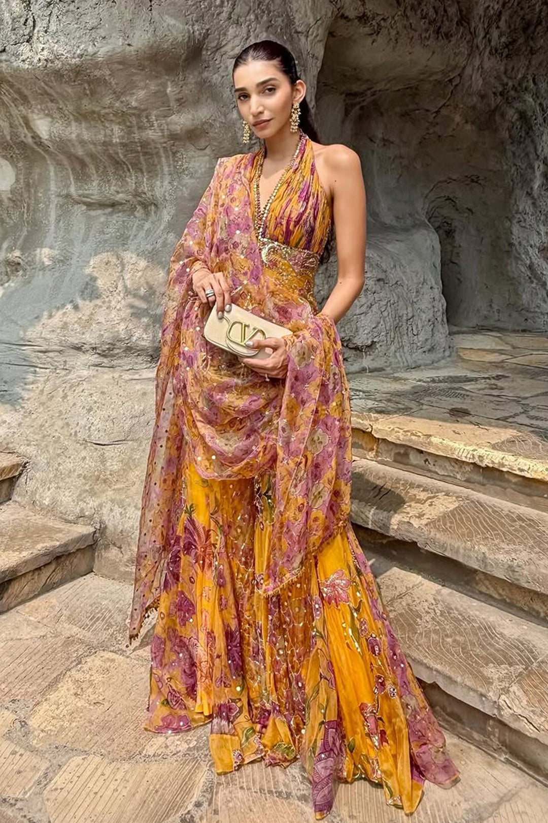 Woman in a floral dress standing on stone steps with a natural rock formation in the background