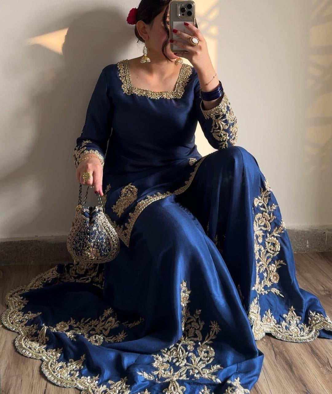Woman in a blue embroidered traditional outfit sitting on the floor.