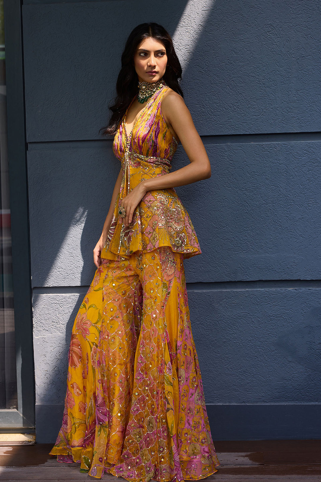 Woman wearing a mustard yellow and pink floral outfit against a blue wall.