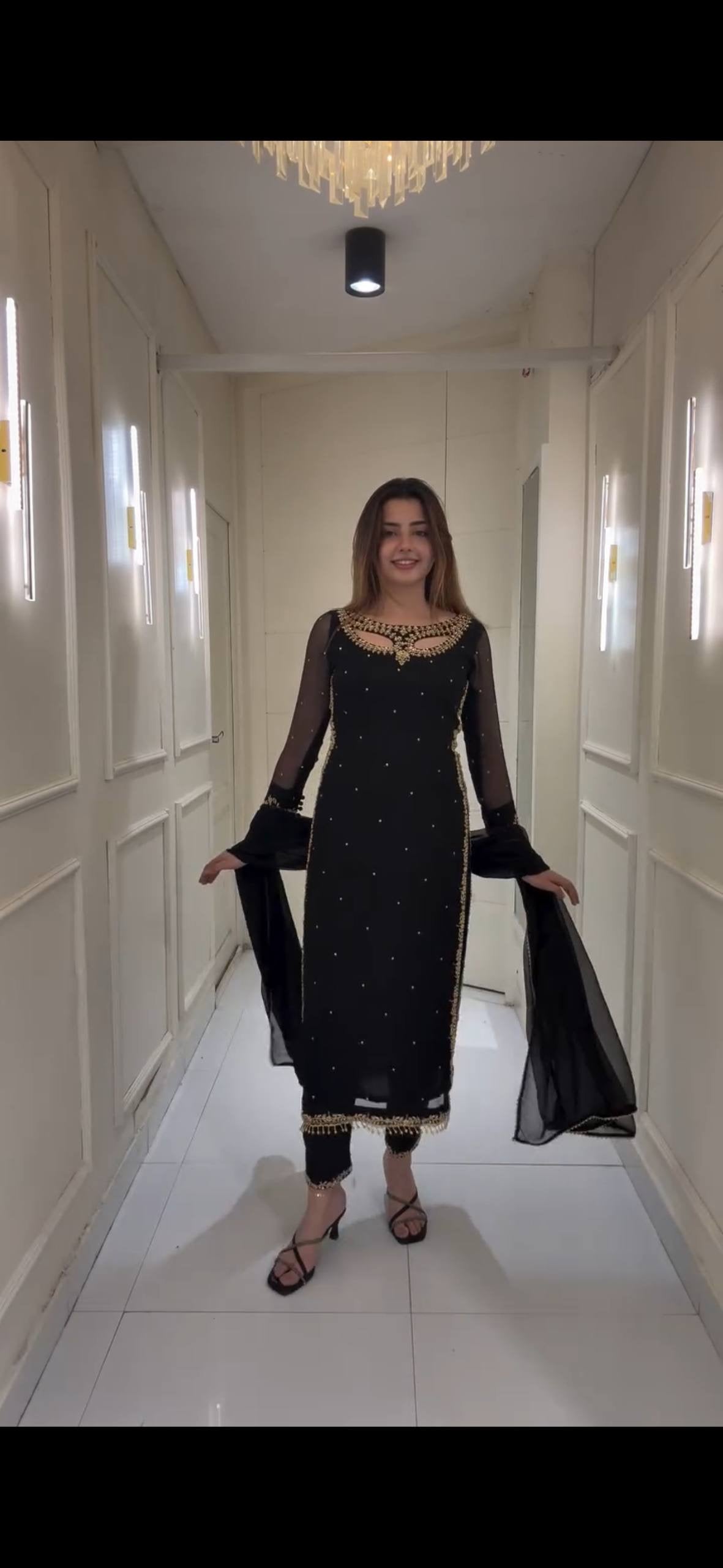 Woman in a black traditional outfit standing in a well-lit hallway.