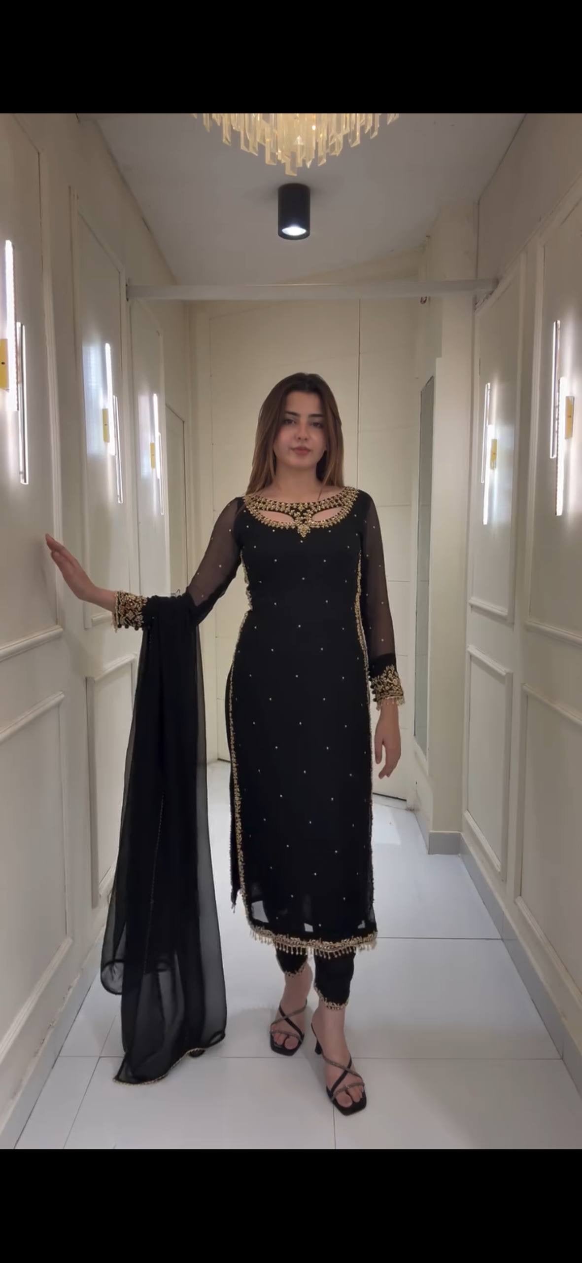 Woman in a black traditional outfit standing in a well-lit hallway.