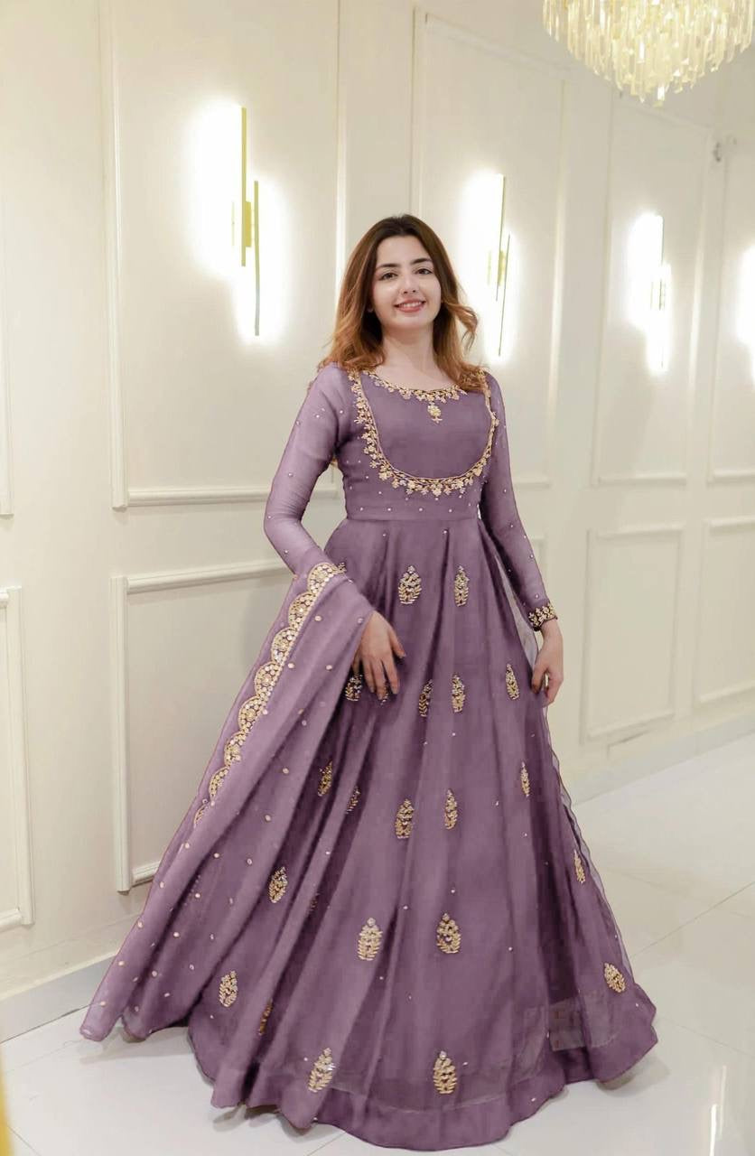 Woman wearing a purple embroidered dress in a white room with a chandelier.