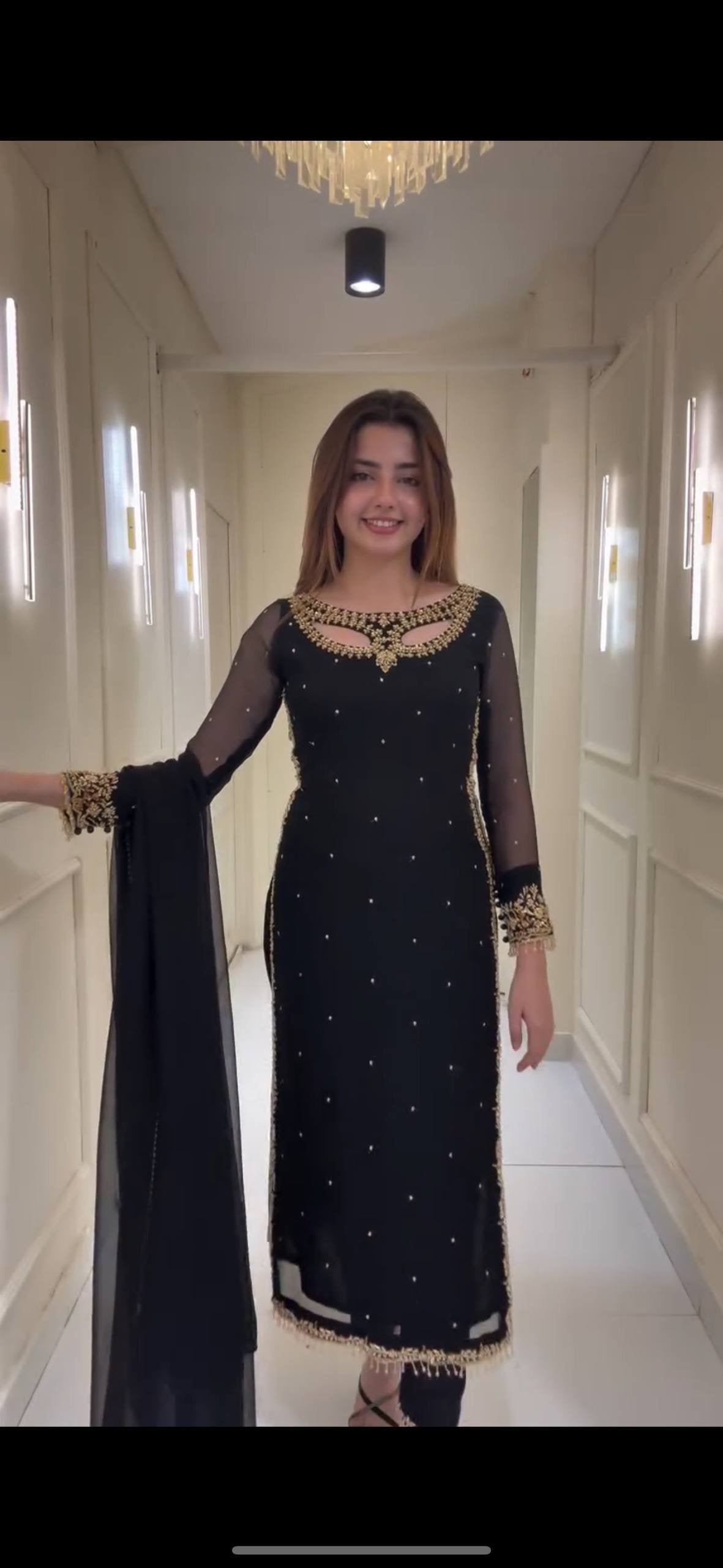 Woman in a black traditional outfit standing in a well-lit hallway.