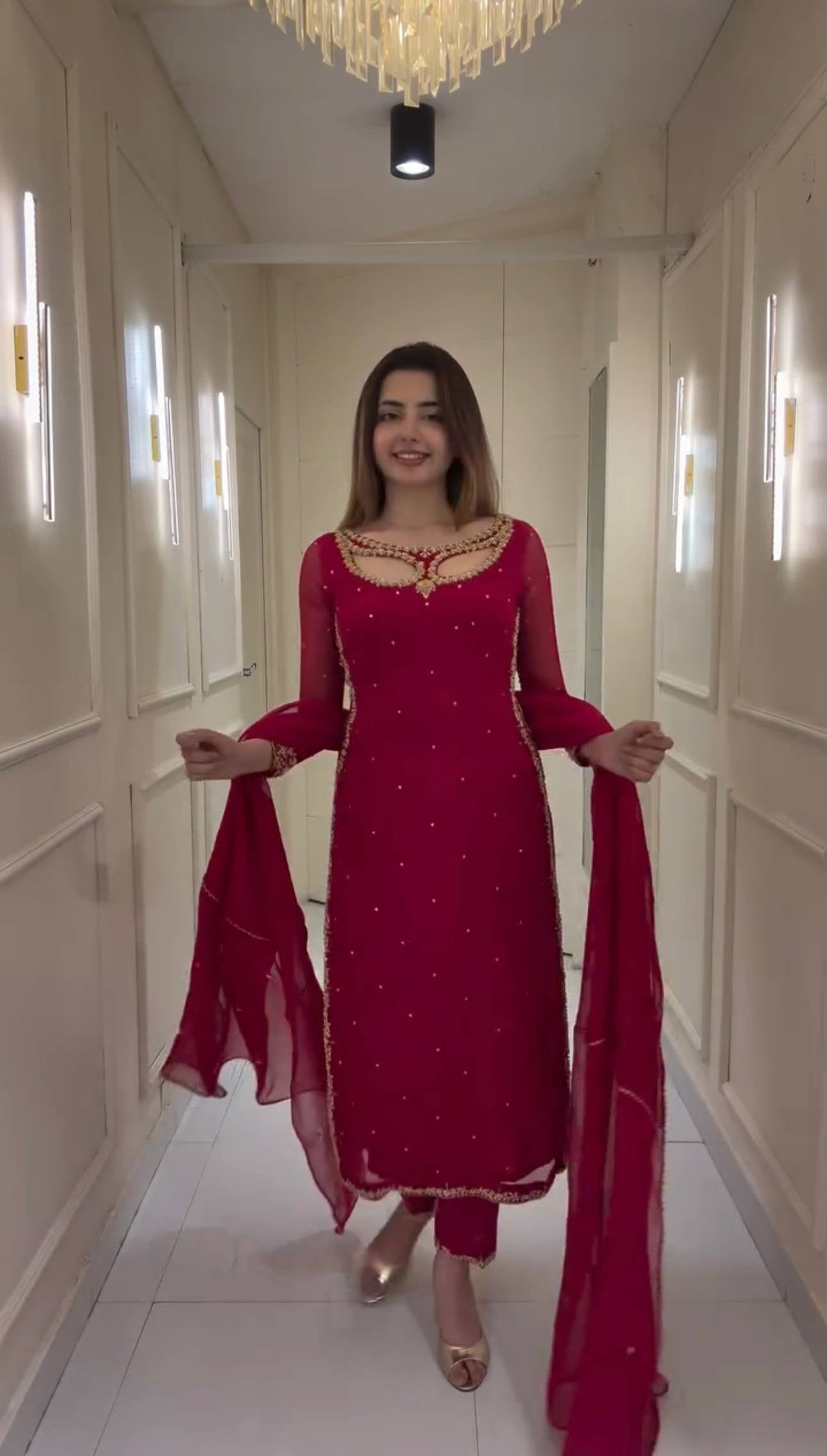 Woman in a red traditional outfit standing in a hallway with white walls and a chandelier.