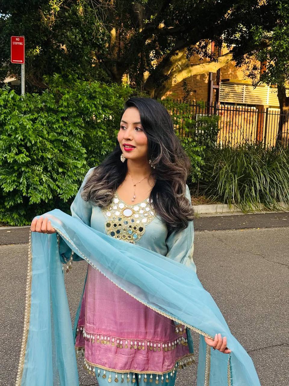 Woman in traditional outfit with a blue dupatta standing outdoors.