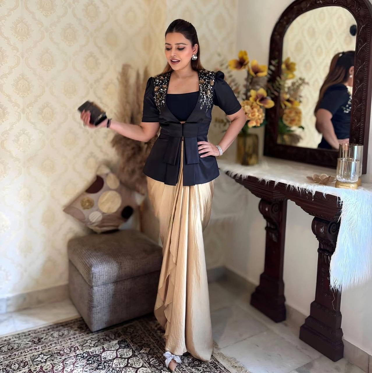 Woman in a black blouse and beige saree standing in front of a mirror.