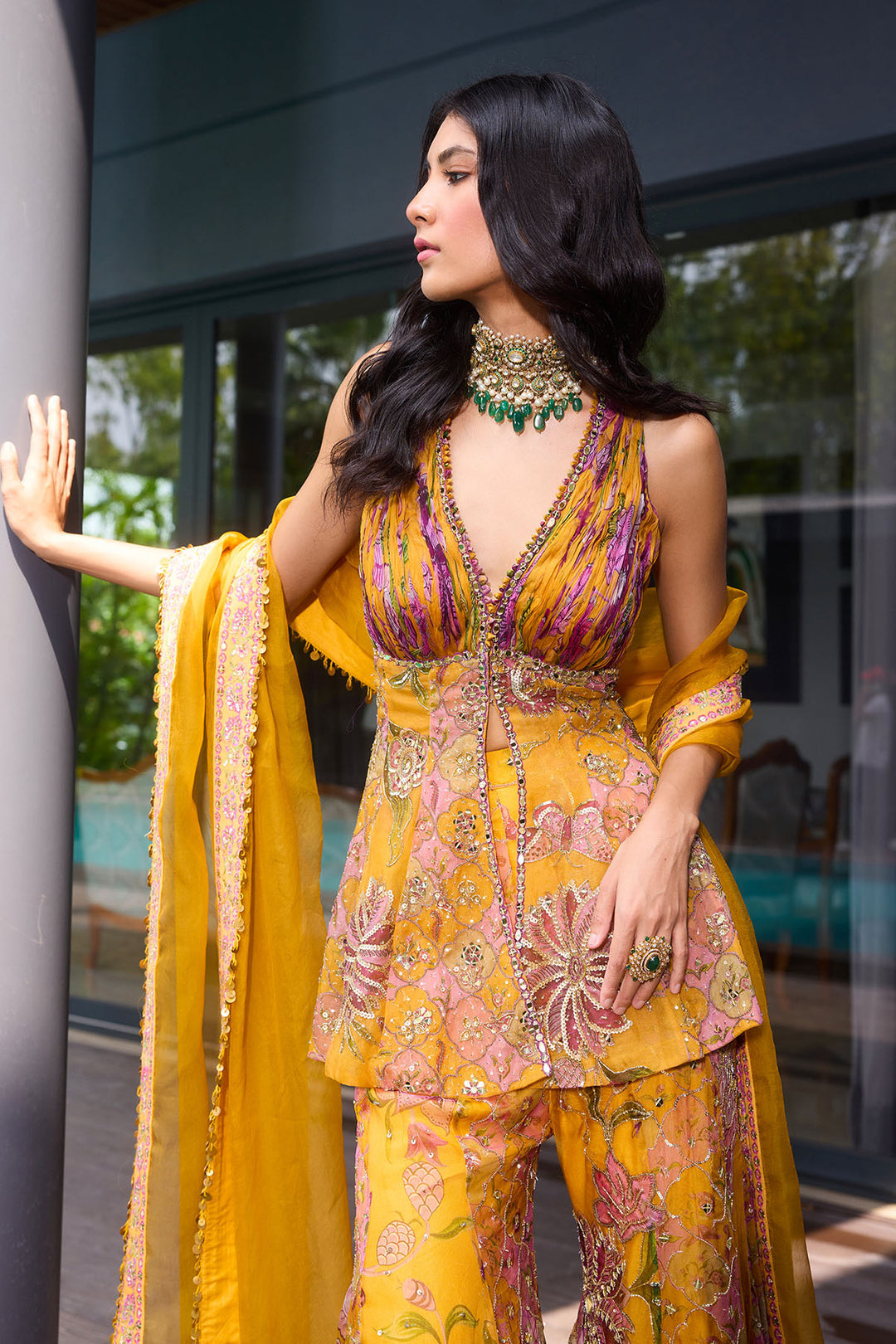 Woman in a yellow and pink traditional outfit with intricate patterns, standing indoors.