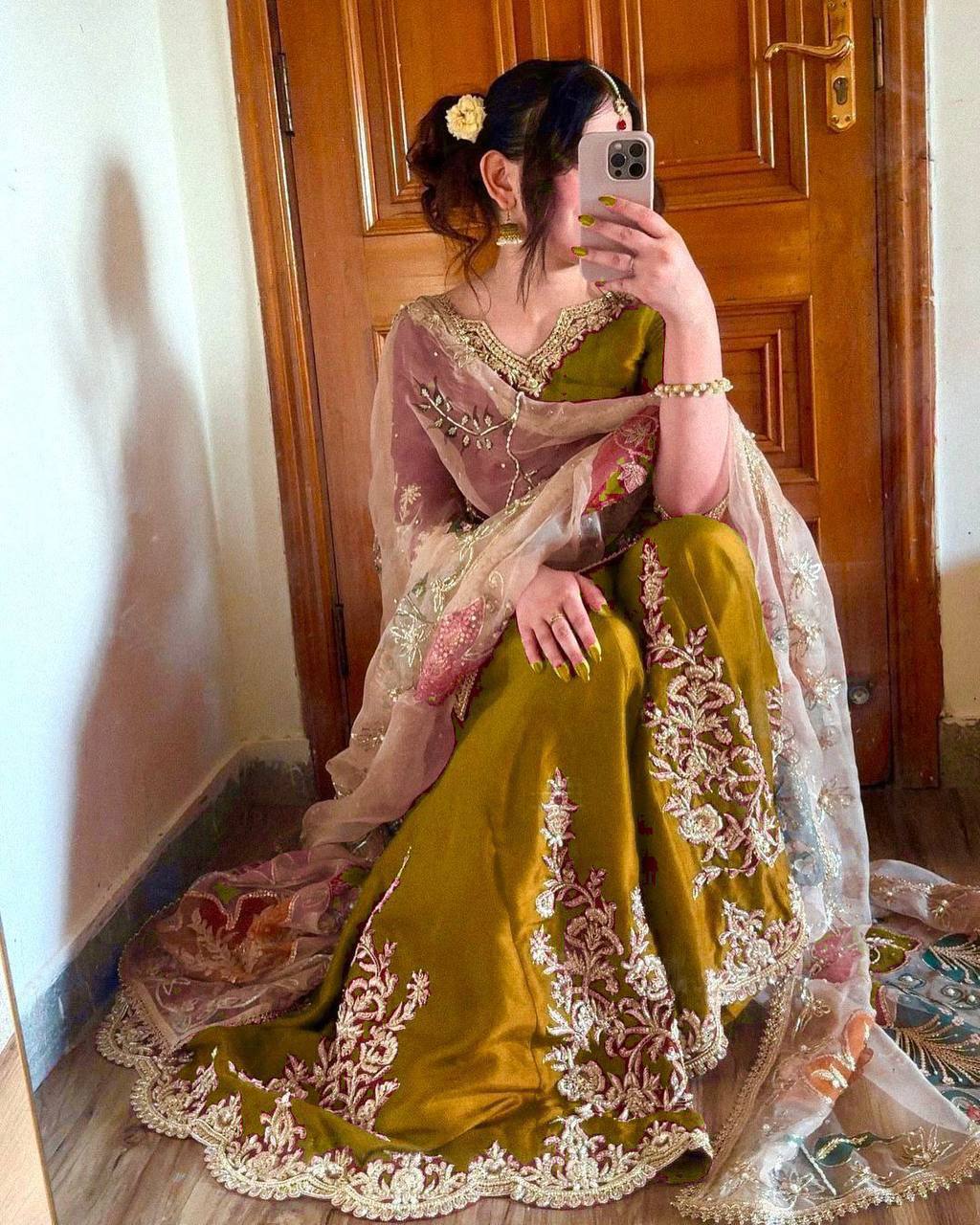 Woman in a green and pink traditional outfit taking a mirror selfie.
