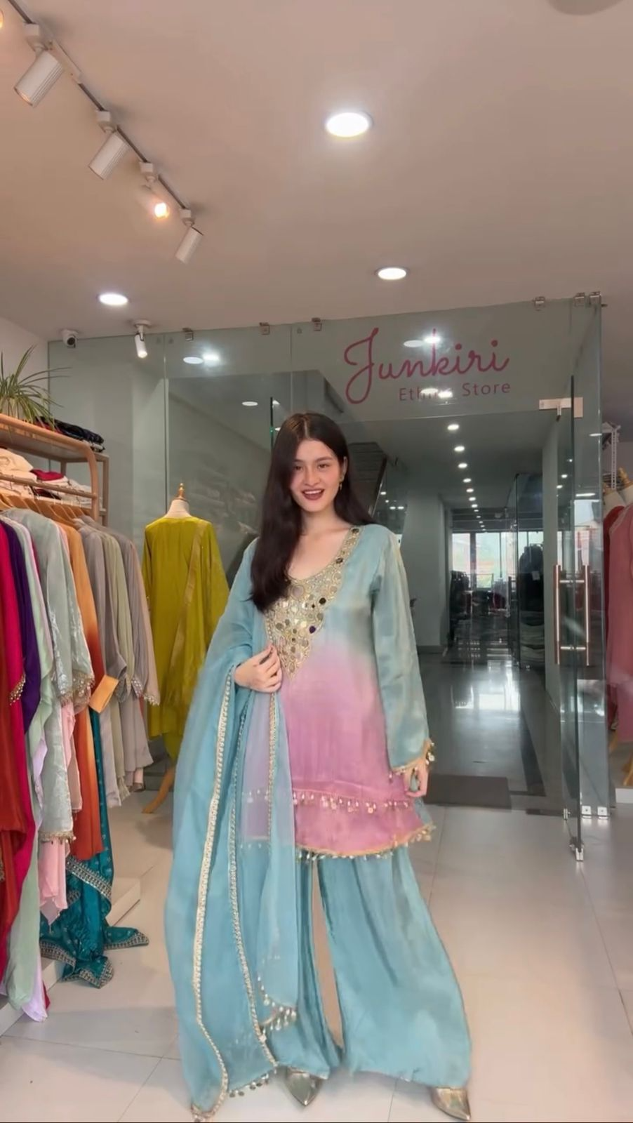 Woman in a light blue and pink traditional outfit standing in a store with 'Junkkiro' branding.