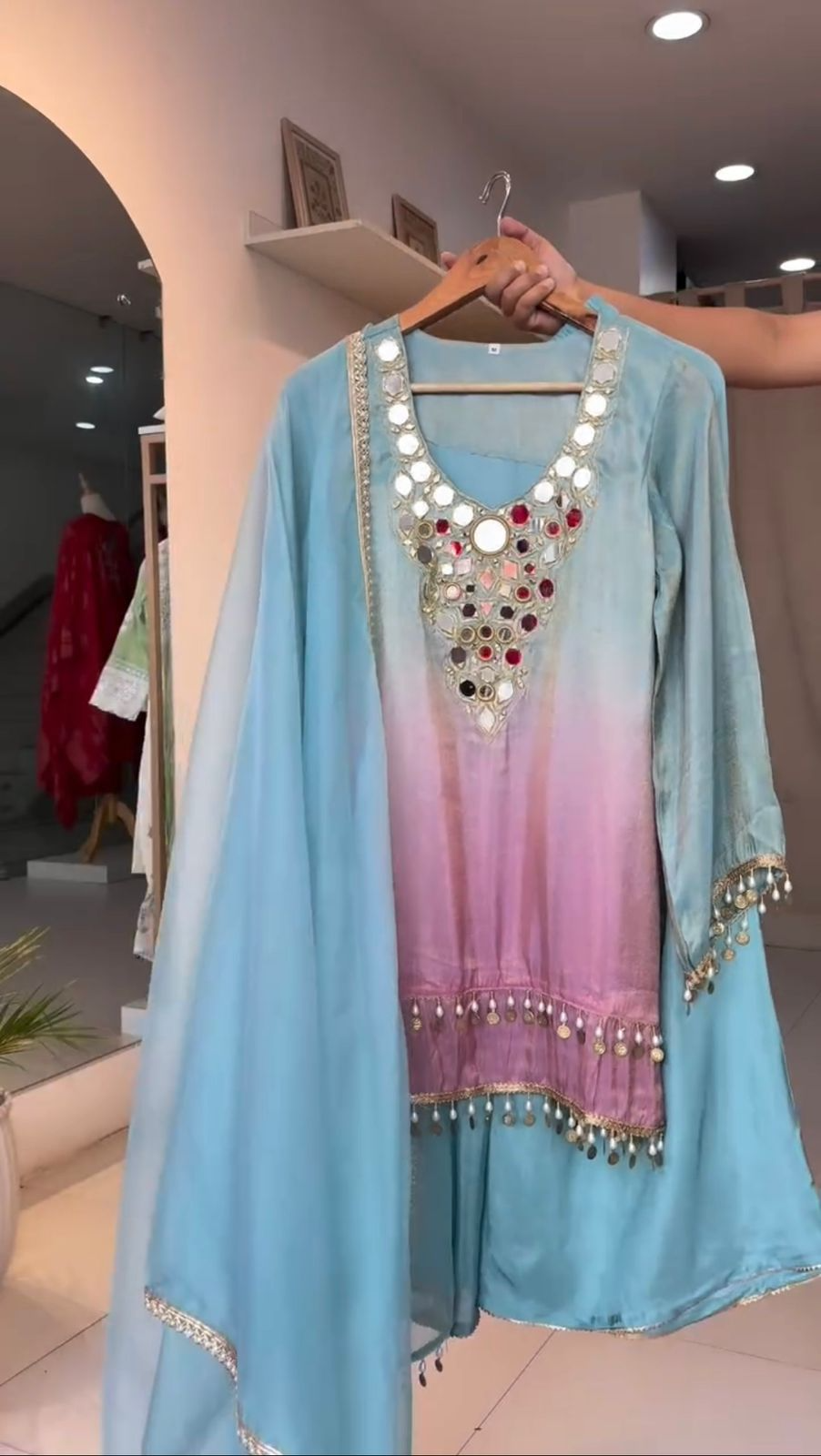 Light blue and pink traditional outfit with embellishments on a hanger indoors.