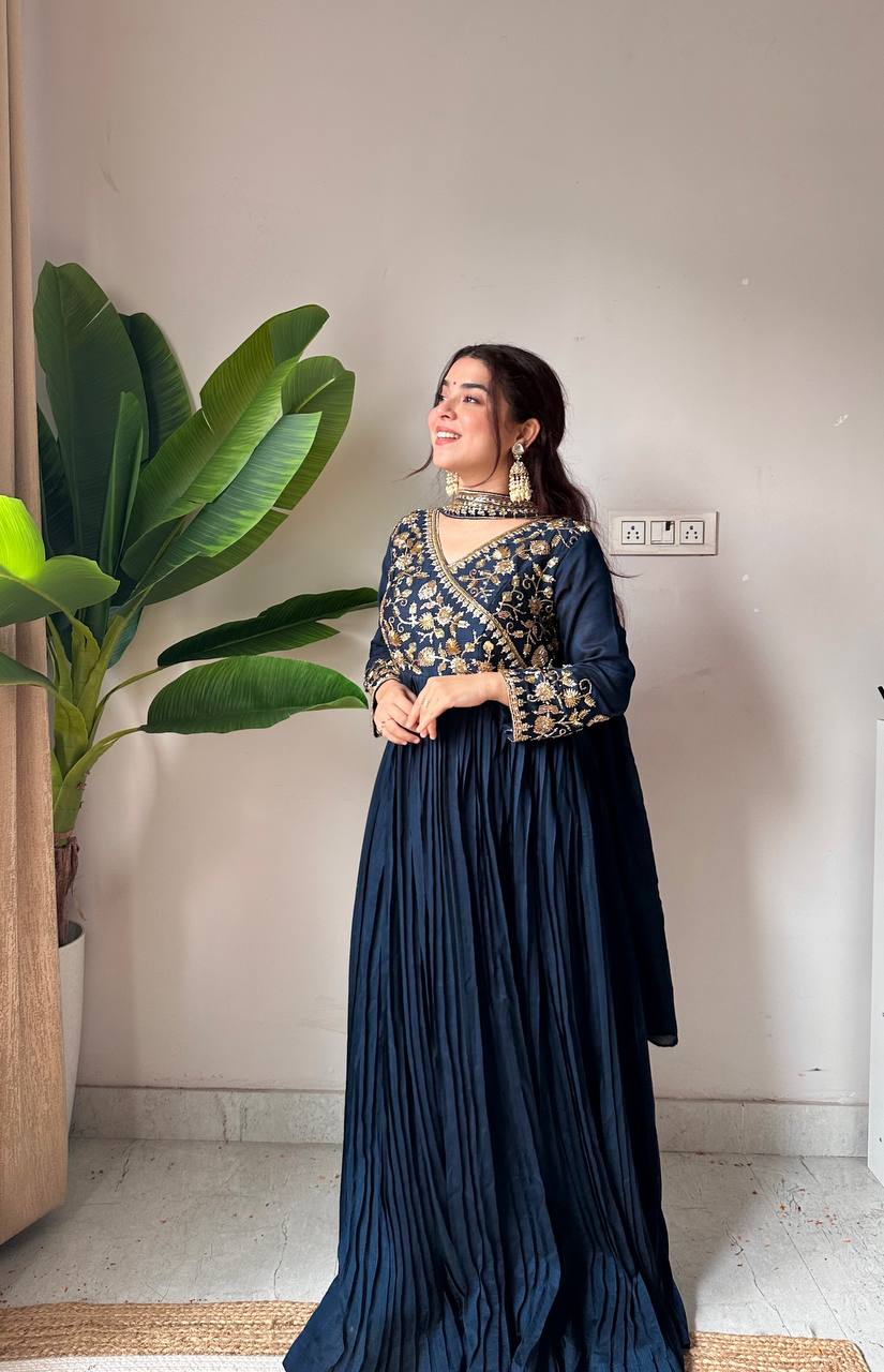 Woman in a dark blue traditional outfit standing indoors with a plant in the background