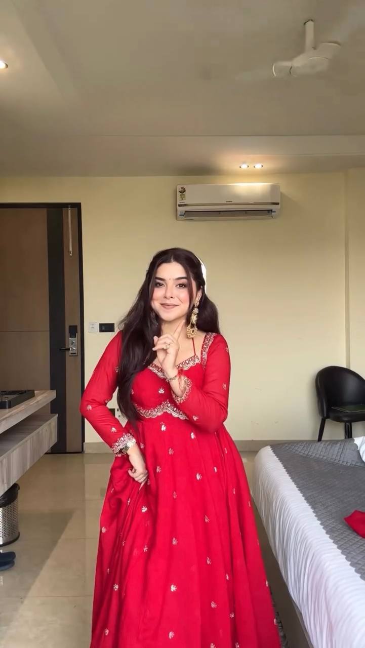 Woman in a red traditional outfit standing in a room with an air conditioner on the wall.