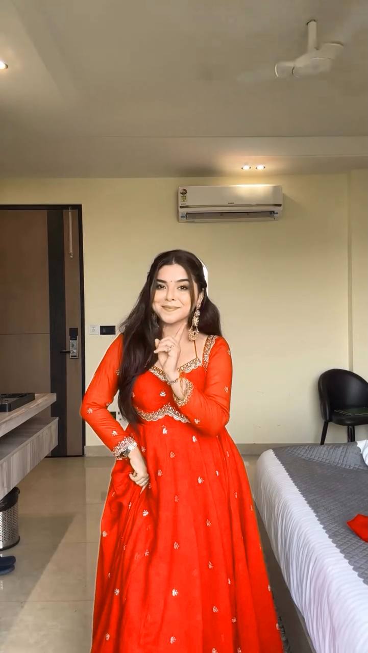 Woman in a red traditional outfit standing in a room with a bed and air conditioner.