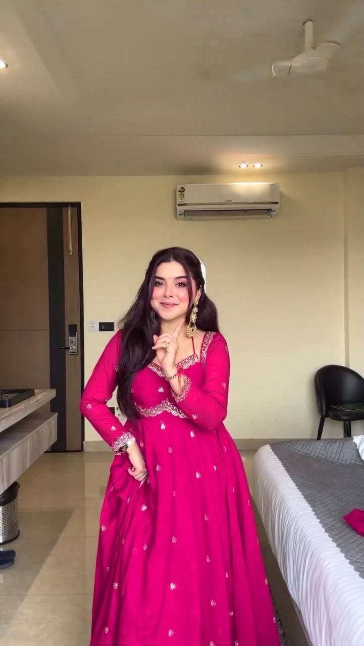 Woman in a pink traditional outfit standing in a room with a bed and air conditioner.
