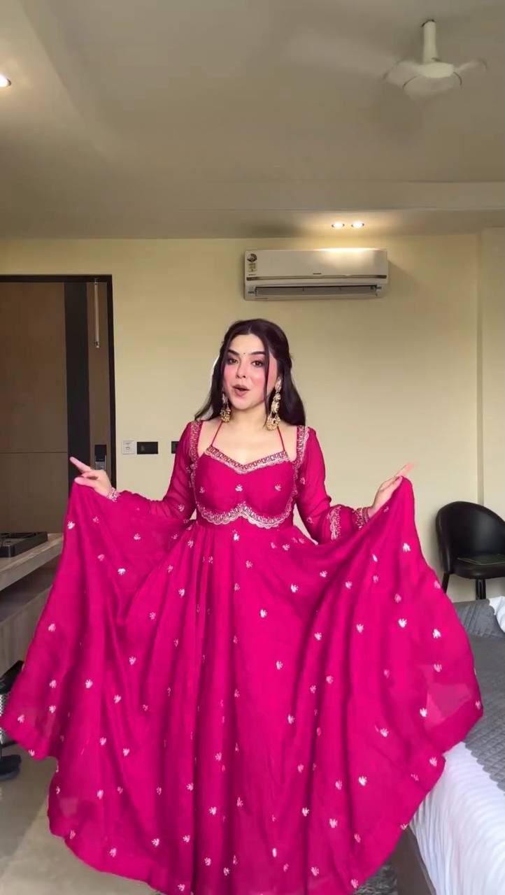 Woman in a bright pink traditional outfit with white patterns in a room.