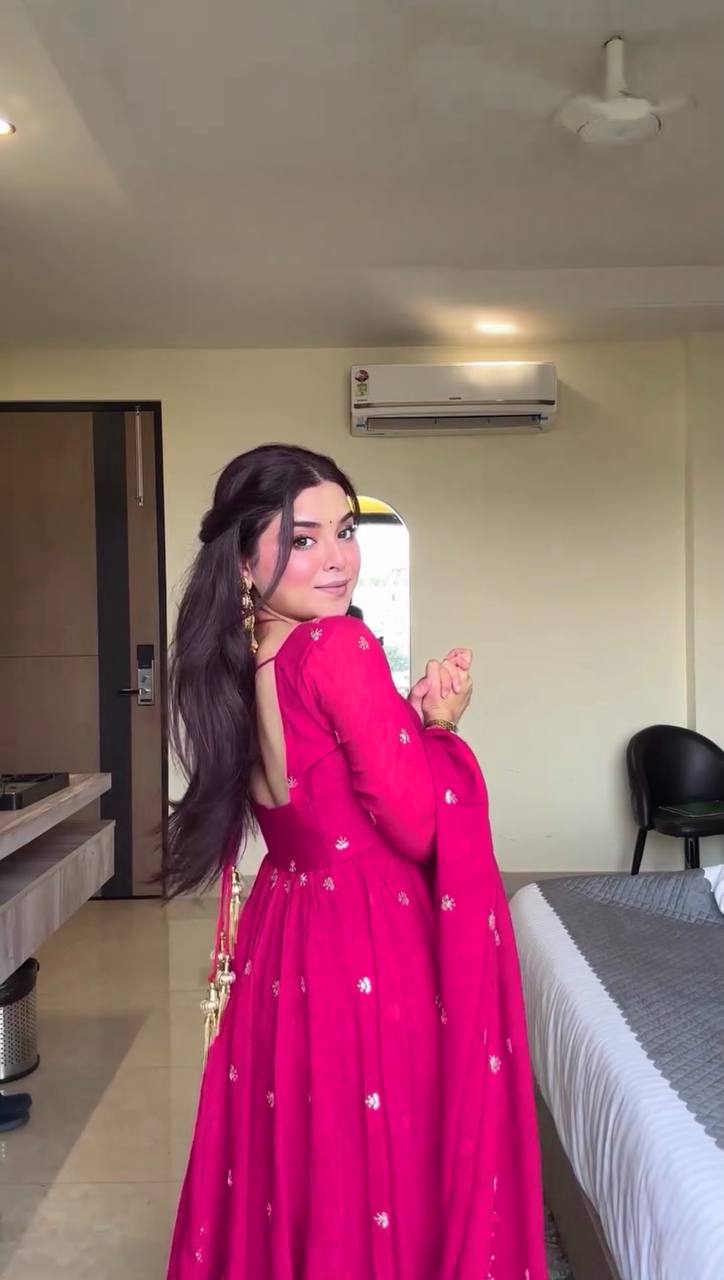 Woman in a pink traditional outfit standing in a room with a bed and air conditioner.