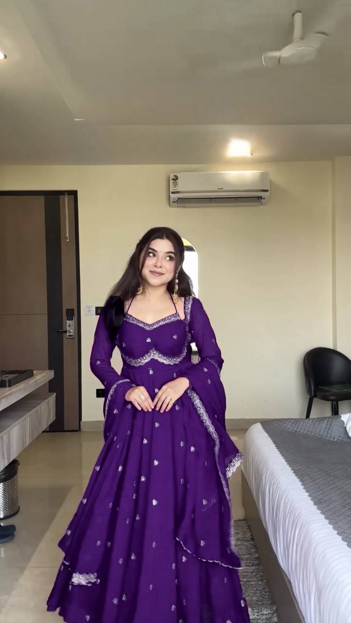 Woman in a purple traditional outfit standing in a room with a bed and air conditioner.