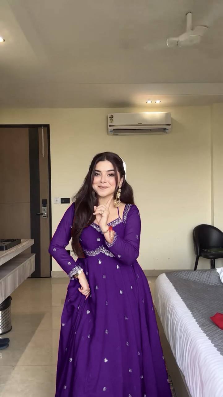 Woman in a purple dress standing in a room with a bed and air conditioner.